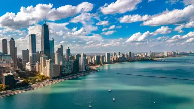 Aerial view of Chicago skyline on bright day with turquoise Lake Michigan in foreground.